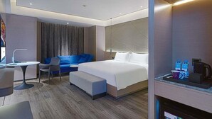 A modern hotel room with a bed, a seating area with a blue sofa, a small table, and a coffee machine.