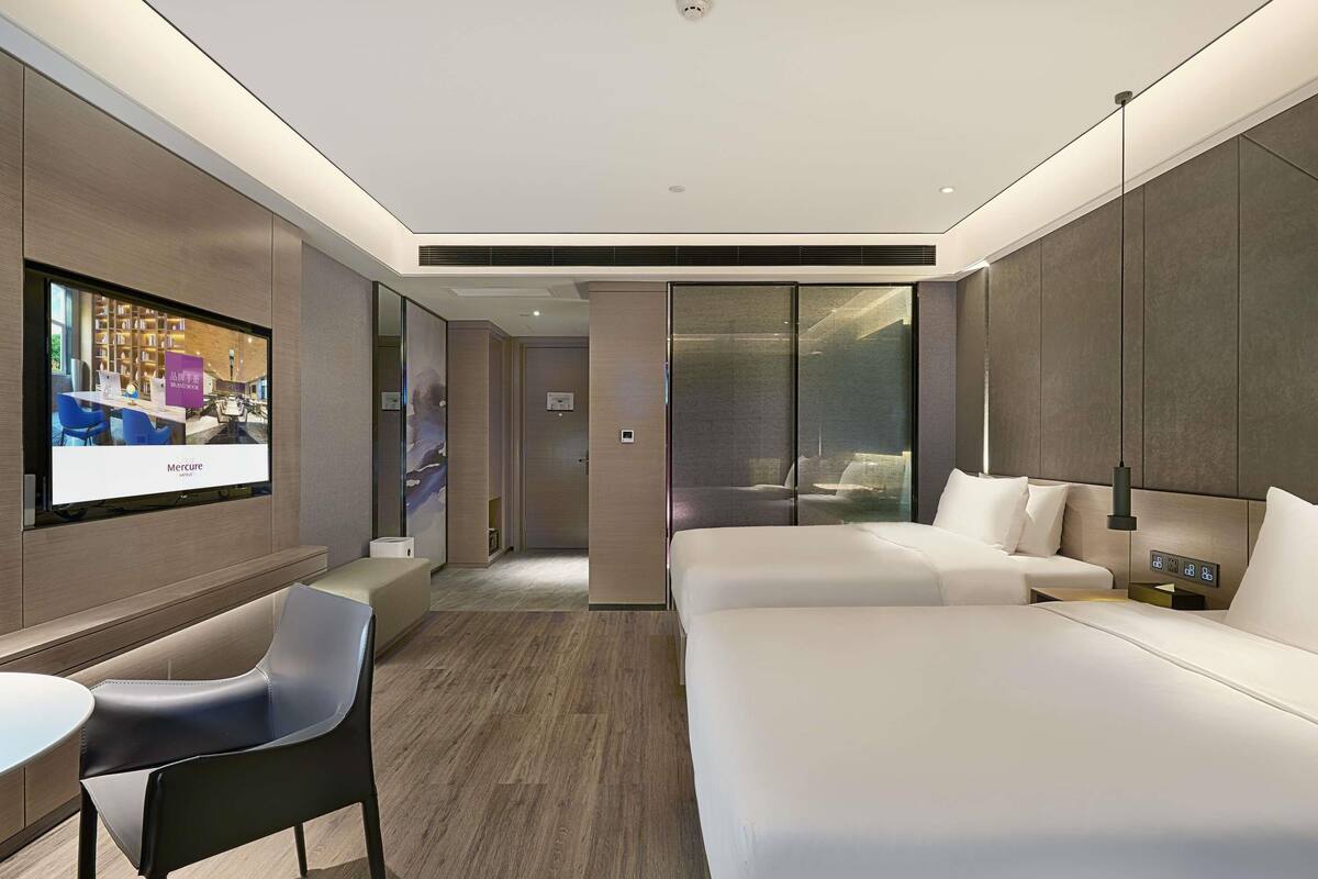 Une chambre d’hôtel moderne, dotée d’un grand lit, d’un bureau, d’une chaise et d’un téléviseur qui diffuse une image de la chambre.