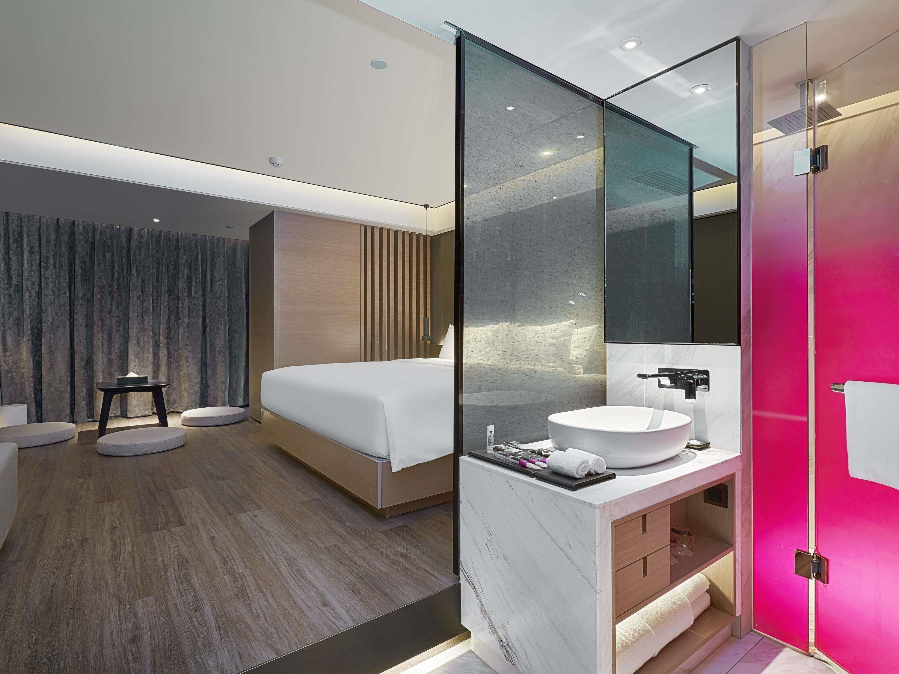 Ein modernes Hotelzimmer mit Bett, Nachttisch und einem Badezimmer mit großem Spiegel, Waschbecken und Dusche.