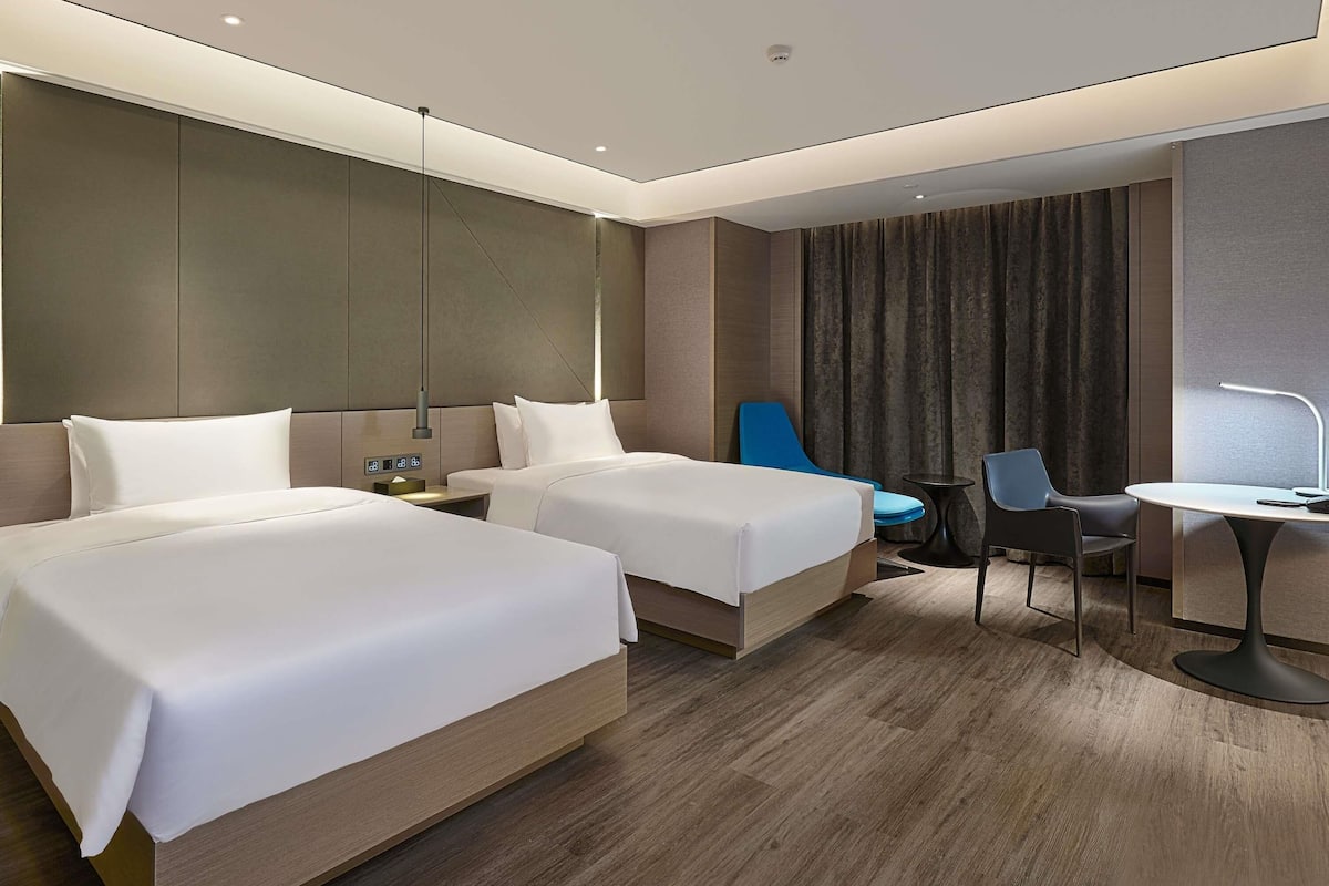 Une chambre d’hôtel avec deux lits, un bureau, une chaise, une petite table et un rideau.