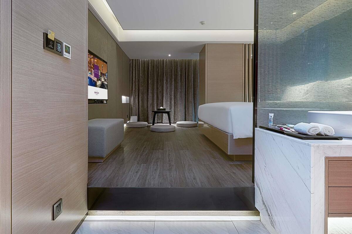 Une chambre d’hôtel moderne comprenant un lit, une petite table, un coin salon et une salle de bain avec baignoire.