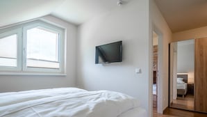 Ett sovrum med en säng, en tv som är monterad på väggen och ett fönster med persienner.
