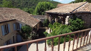 A traditional stone building with a tiled roof, a wooden balcony railing, and lush greenery in the background. - Holiday Home in Ardeche Near Chateau de Ventadour (Lalevade-d'Ardeche)