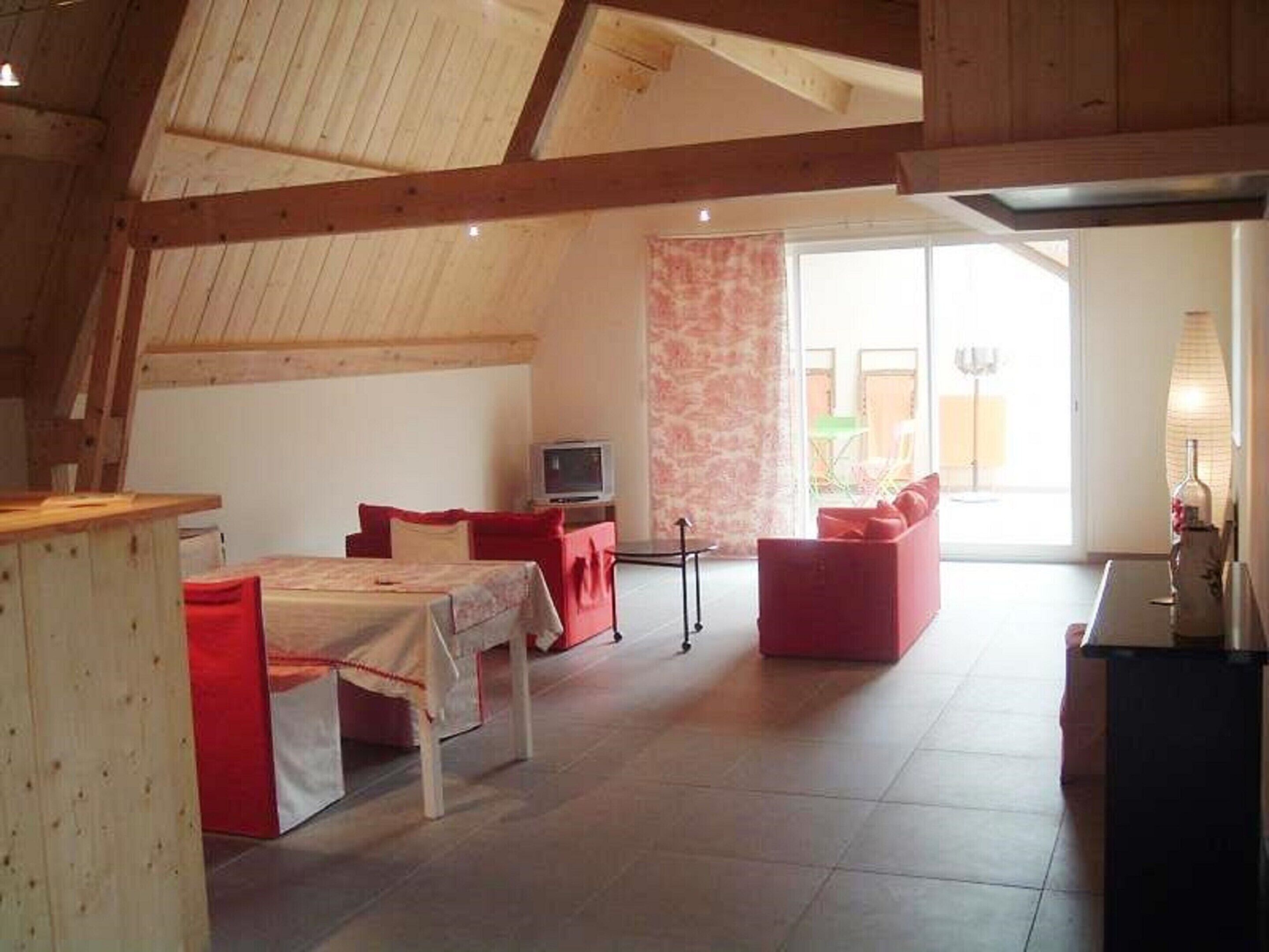 A spacious loft bedroom with a high ceiling, a bed, a desk, and a seating area with red furniture.