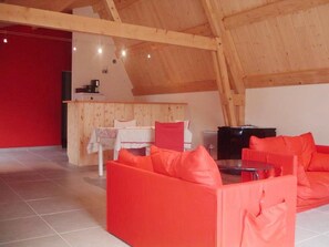 A high-ceilinged room with a wooden ceiling and walls, a red sofa, a small table, and a kitchen area with a stove. - Holiday Home in Ardeche Near Chateau de Ventadour (Lalevade-d'Ardeche)