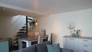 A modern interior with a sofa, dining table, chairs, and a staircase. - Holiday Home in Egmond by the Beach (Egmond aan Zee)