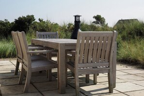 Een houten tuinset met tafel en stoelen op een stenen terras, met een zwarte lantaarn op de achtergrond.