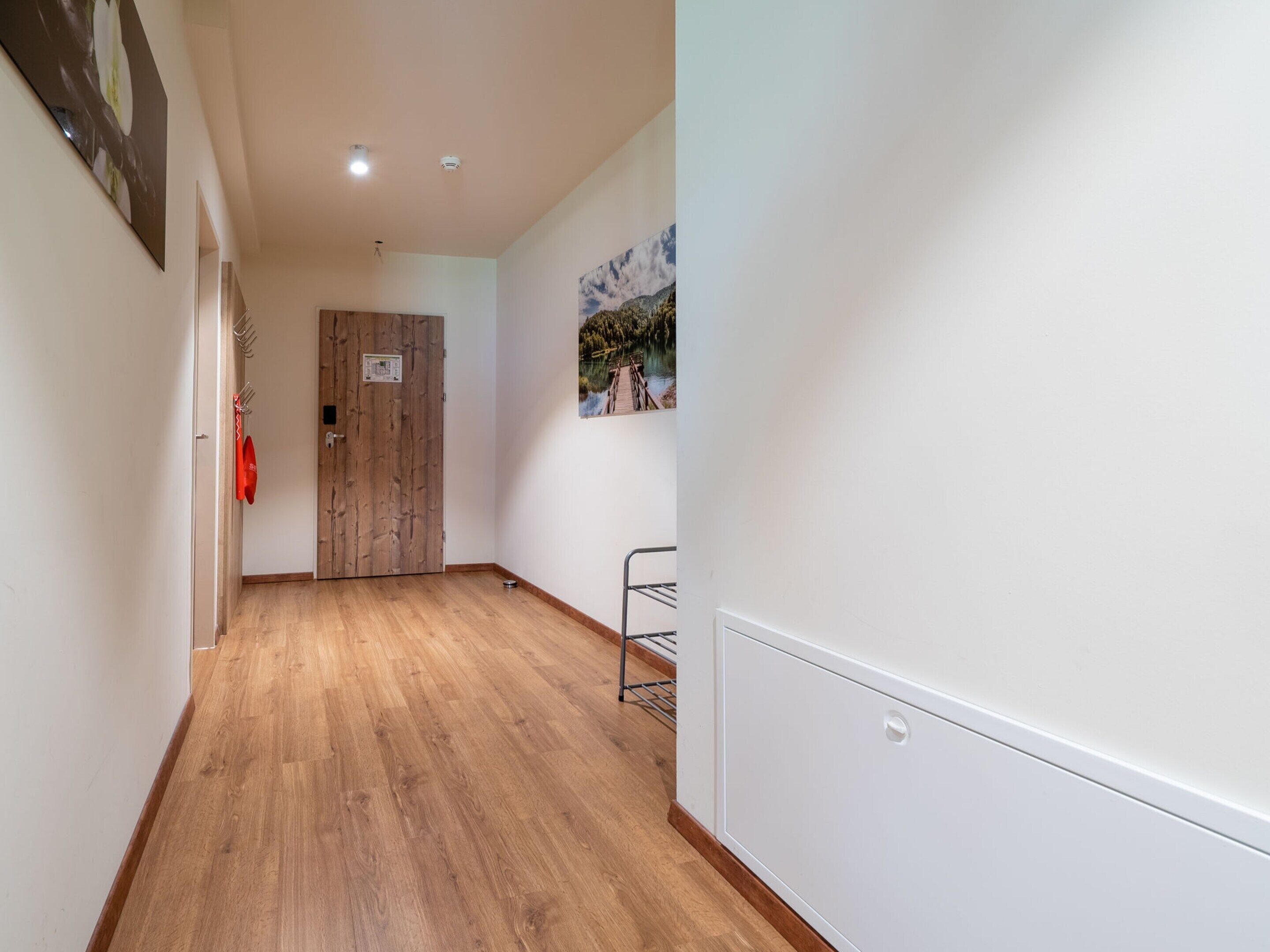 A hallway with wooden flooring, a coat rack, and a door with a sign.