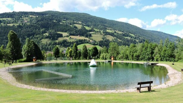 A serene lake with a bench and a small boat, surrounded by lush greenery and hills in the background. - Chalet in Stadl an der Mur / Styria With Terrace (Stadl-Predlitz)
