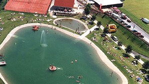An aerial view of a park with a large pond, picnic areas, and a tennis court. - Chalet in Stadl an der Mur / Styria With Terrace (Stadl-Predlitz)