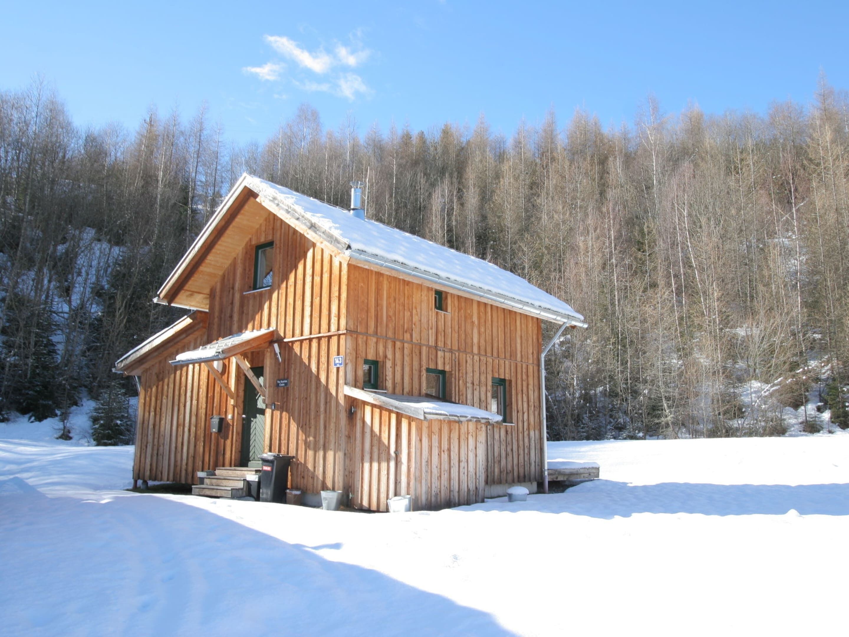 A wooden cabin with a steeply pitched roof, a chimney, and a small porch with steps leading up to the entrance.