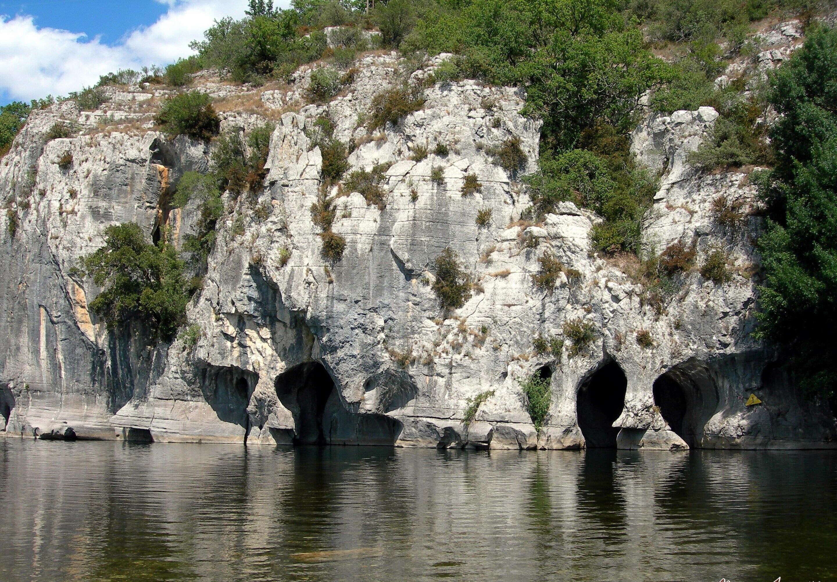 A rocky cliff with natural rock formations and a calm body of water.