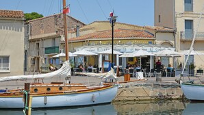 Restaurante à beira-mar com mesas ao ar livre, barcos atracados por perto e arquitetura tradicional.