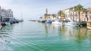 Uma marina com barcos atracados na água, edifícios com varandas e uma torre imponente ao longe.