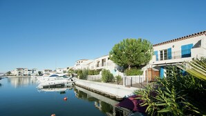 Uma marina com barcos atracados, um corpo d'água calma e edifícios com persianas azuis.