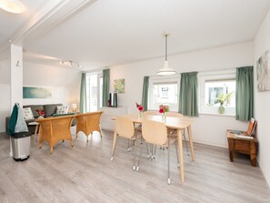 Un salon moderne comprenant un coin repas, un canapé, un téléviseur et une petite table sur laquelle est posé un vase de fleurs.