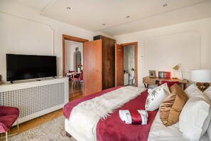 A modern bedroom with a large bed, a TV, a desk, and a wardrobe.