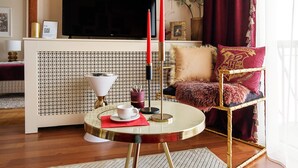 Ein Wohnzimmer mit Fernseher, einer roten Kerze, einem runden Tisch mit einer weißen Tasse und einem roten und goldenen Sessel.