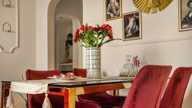 Ein Esstisch mit einer Vase roter Blumen, roten Samtstühlen und einer Wand mit gerahmten Bildern.