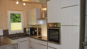 Een moderne keuken met witte kasten, een ingebouwde oven en een raam met jaloezieën.
