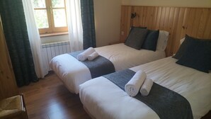 Two single beds with white linens and dark gray headboards in a room with wooden floors and a window with curtains.