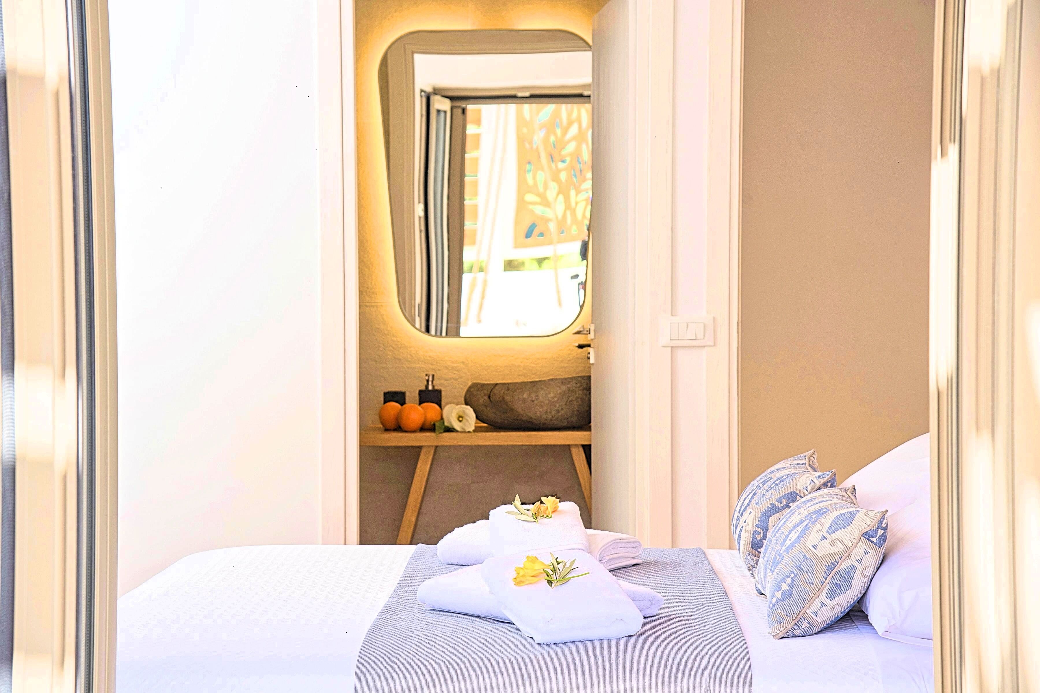 A bedroom with a bed, pillows, a towel, a mirror, and a shelf with toiletries.