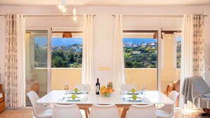 Un coin repas avec une table dressée pour quatre personnes, un saladier de fruits et une bouteille de vin.