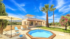 Un espace aménagé au bord de la piscine, avec des chaises longues et une piscine, le tout entouré d’une maison et de palmiers.