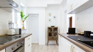 A modern kitchen with white cabinetry, a wooden countertop, and a built-in oven. There is a small wooden cabinet with glass doors and a potted plant on the countertop.