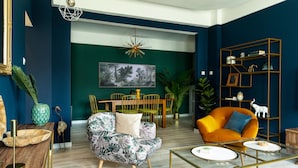 A modern living room with a green accent wall, a dining area with a wooden table and chairs, and a bright orange armchair.