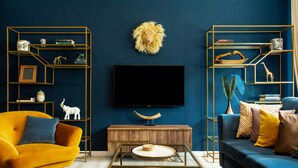 A modern living room with a blue wall, a wooden cabinet, a yellow armchair, a blue sofa, and a TV on the wall. - Welcome to the Jungle (Bucharest)
