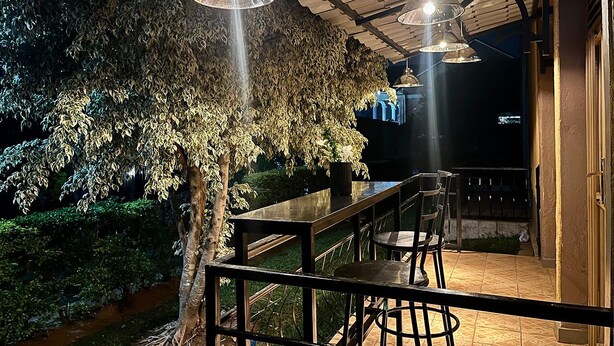 Une terrasse extérieure avec une table et des chaises en bois, entourée d’un jardin luxuriant et d’une pergola en bois.