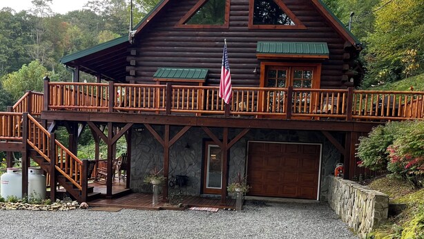 Uma cabana de toras com varanda, base de pedra e uma bandeira americana.