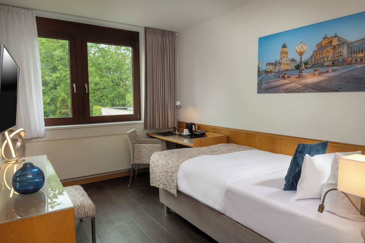 Una habitación de hotel con cama, escritorio, silla, televisor y un cuadro de un paisaje urbano.
