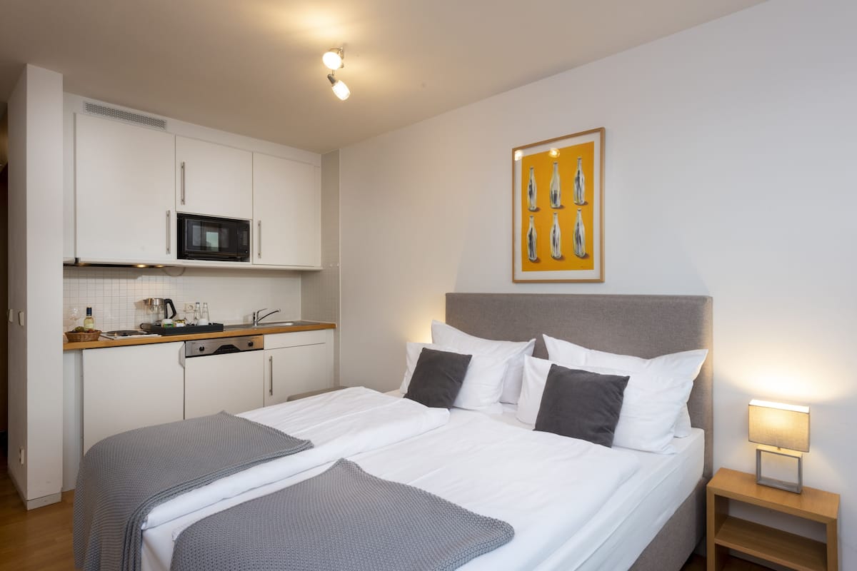 Habitación de hotel con cama, mesita de noche y un área de kitchenette que incluye un microondas y un lavabo.