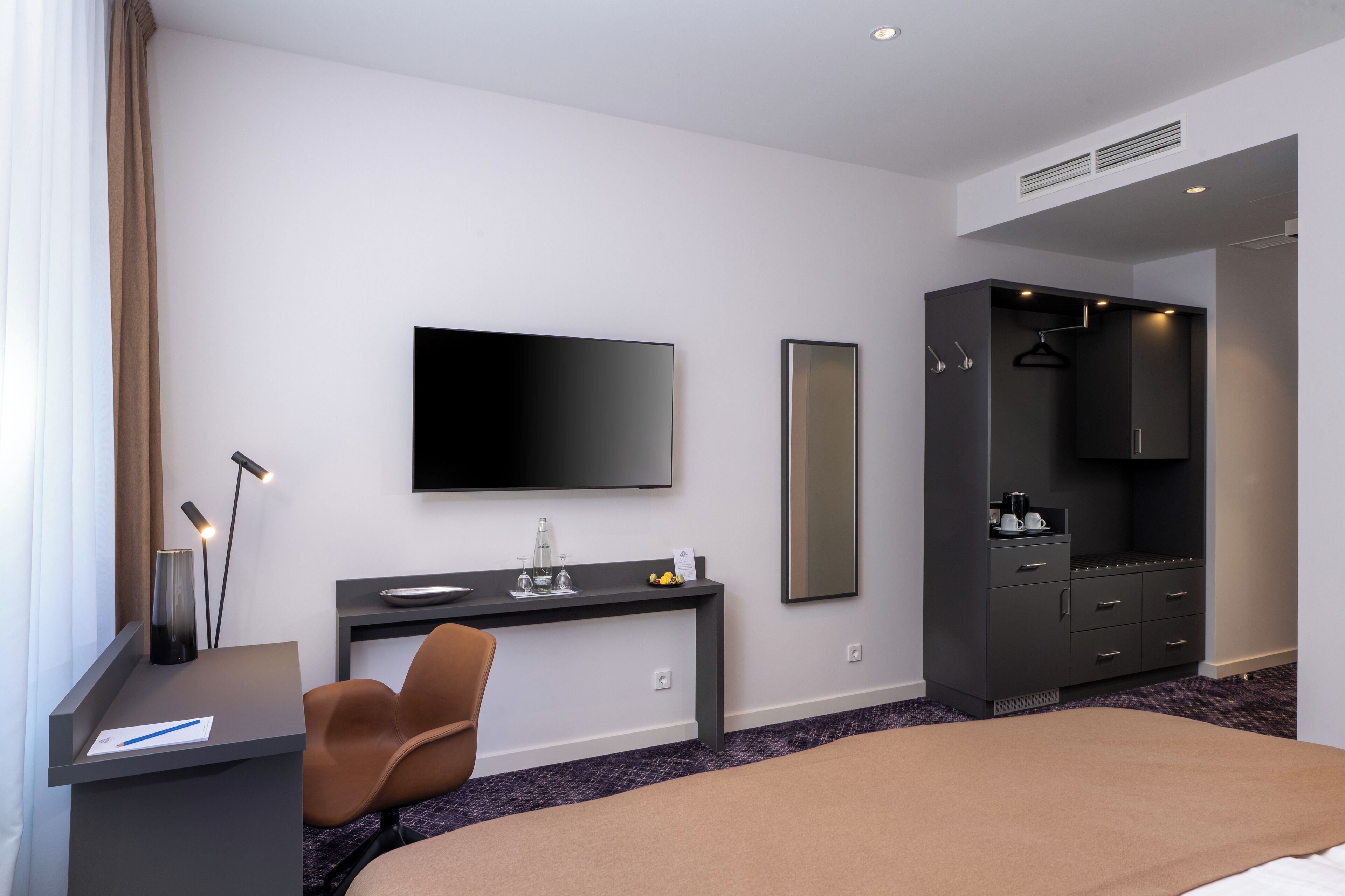 Una camera d'albergo moderna con un letto, una scrivania, una sedia, una TV a schermo piatto, un armadio e uno specchio.
