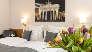A hotel room with a large bed, two bedside lamps, a painting of a building, and a vase of tulips.