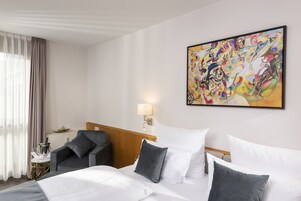 Una habitación de hotel con una cama, una silla, una lámpara y un cuadro en la pared.