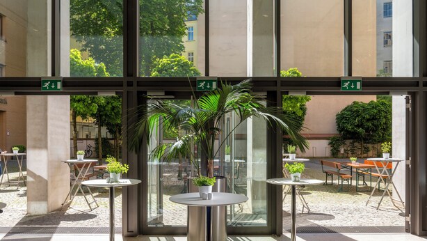 Um pátio interno moderno com paredes de vidro, plantas em vasos e mobiliário para áreas externas.