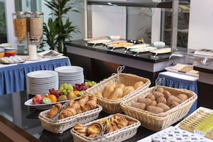 A buffet with various food items including fruits, pastries, and bread.