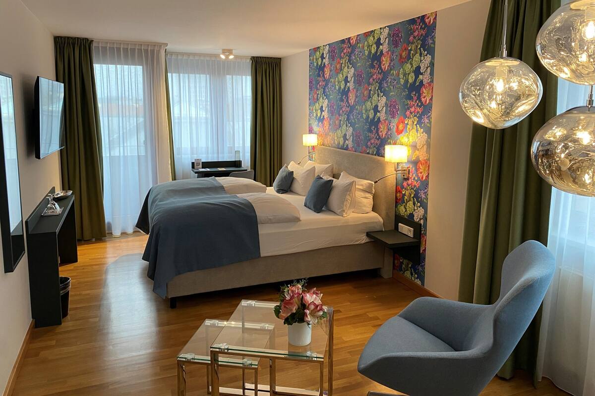 Una habitación de hotel con una cama, un escritorio, una silla, un televisor y un papel tapiz floral.