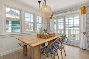 A dining area with a wooden table, wicker chairs, and a hanging light fixture. - Twenty Shore - 3 Sun Suite (Ogunquit)