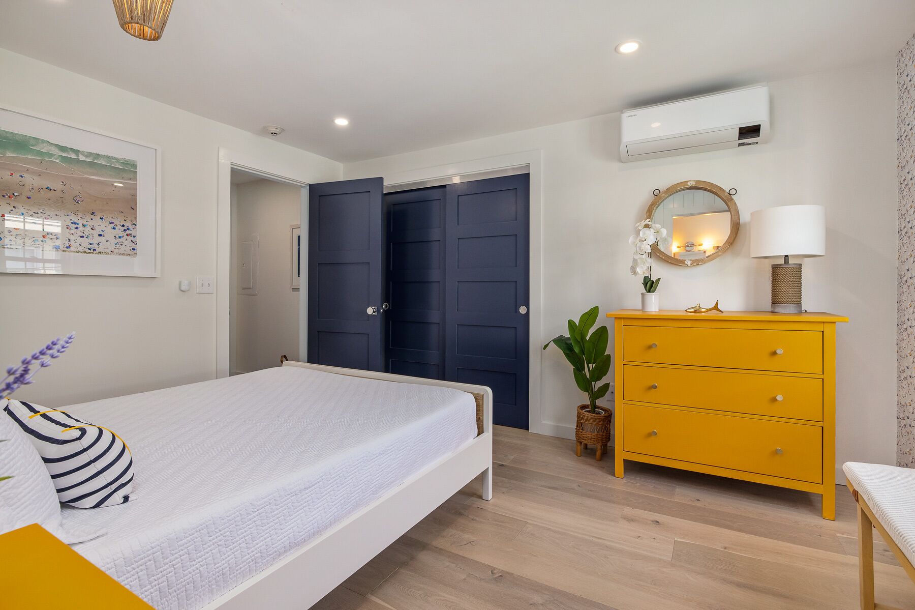 A bedroom with a bed, a dresser, a mirror, and a wall-mounted air conditioner.