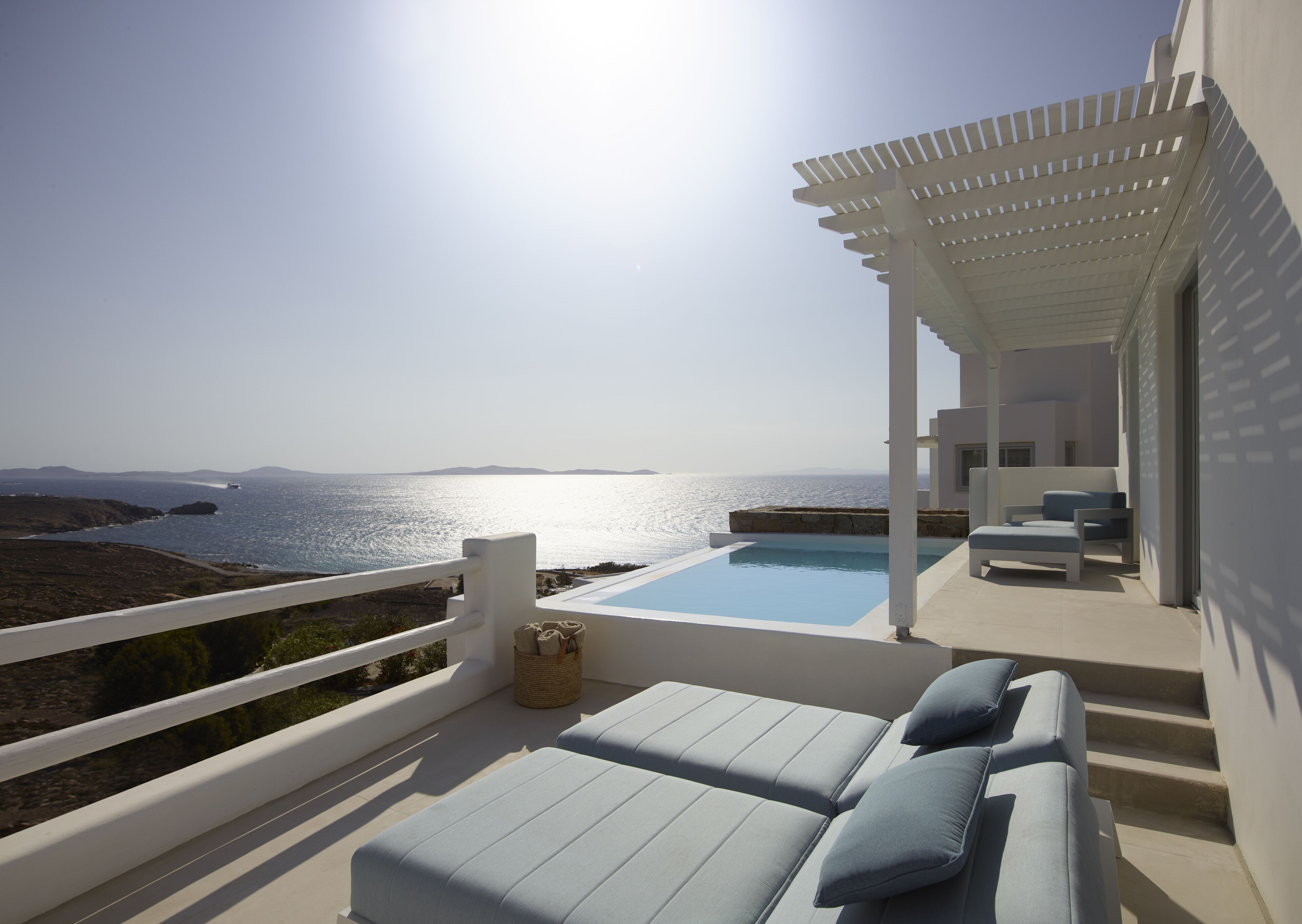 Eine sonnendurchflutete Terrasse mit Pool, Liegestühlen und Meerblick.