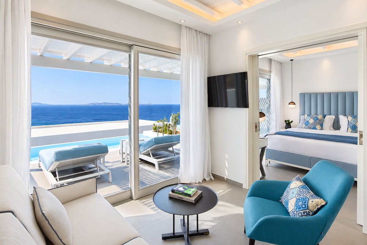 A modern hotel room with a balcony, a bed, a sofa, a coffee table, and a TV.
