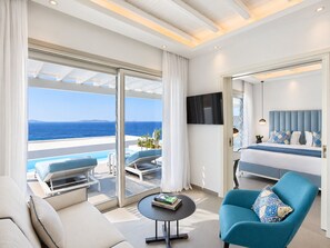 A modern hotel room with a balcony, a bed, a sofa, a coffee table, and a TV. - Epic Blue Mykonos (Mykonos)