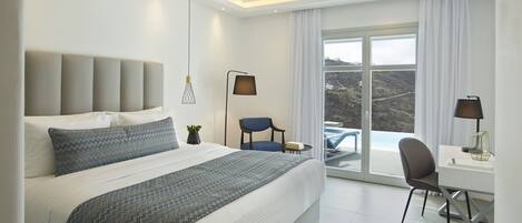 A modern hotel room with a large bed, a desk, and a chair. There is a view of the outdoors through a large window.