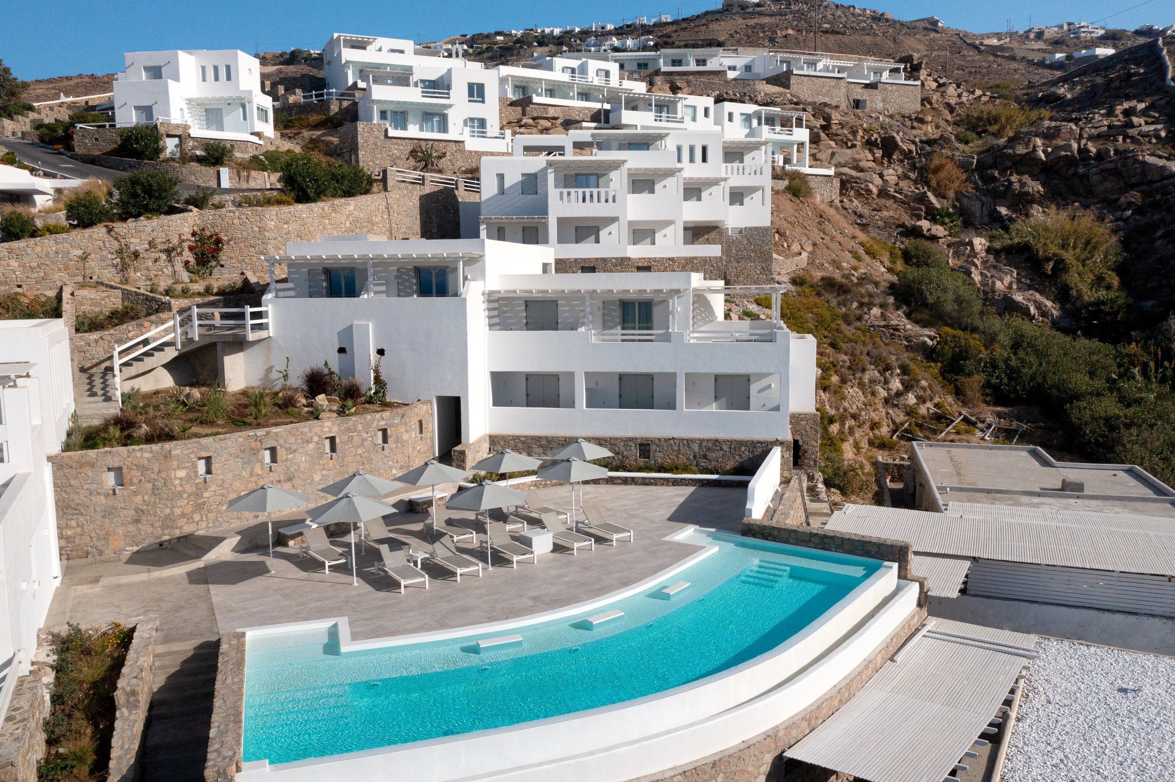 A modern resort with a pool, white buildings, and a mountainous backdrop.