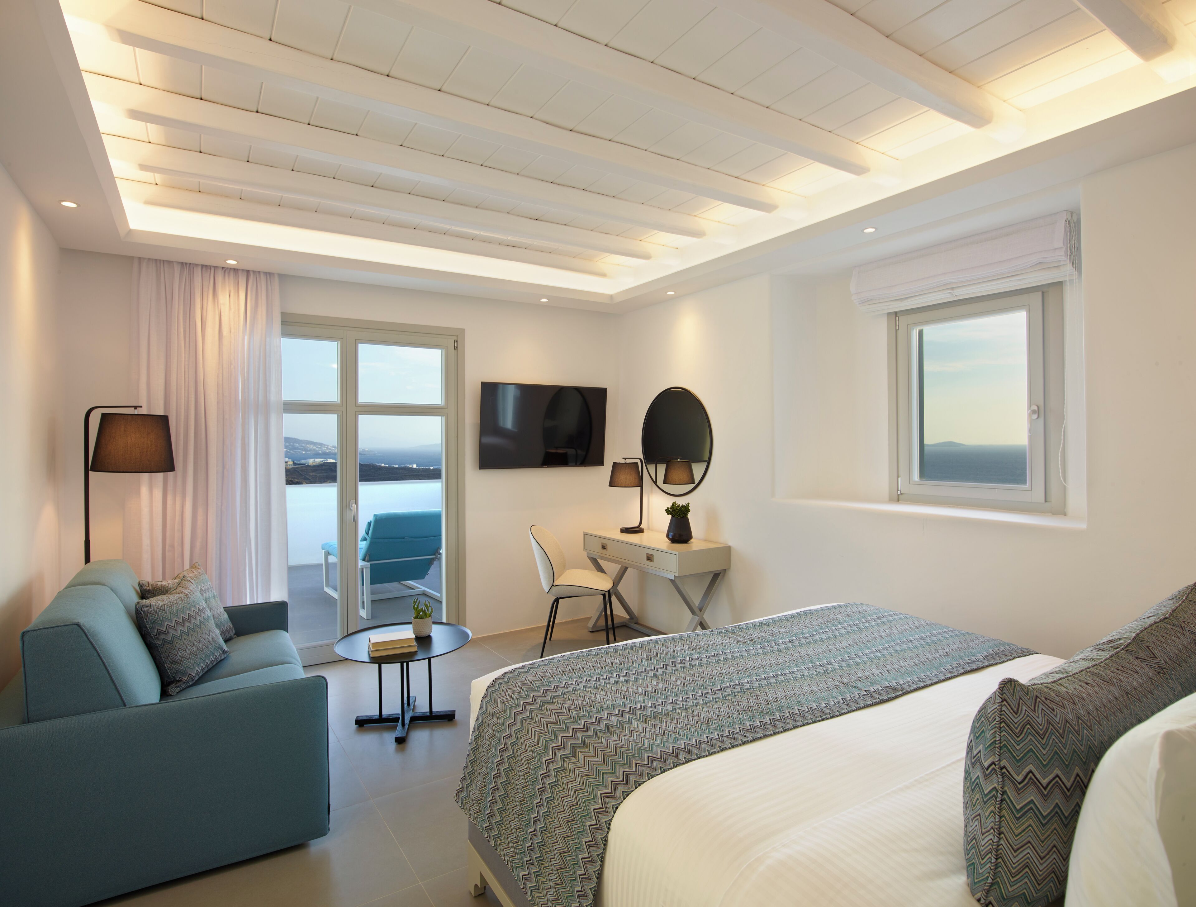 Una habitación de hotel moderna con cama, sofá, escritorio, silla, televisor y ventana con vistas.