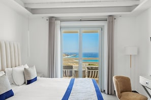 A hotel room with a large bed, a chair, a desk, and a view of the ocean. - Epic Blue Mykonos (Mykonos)